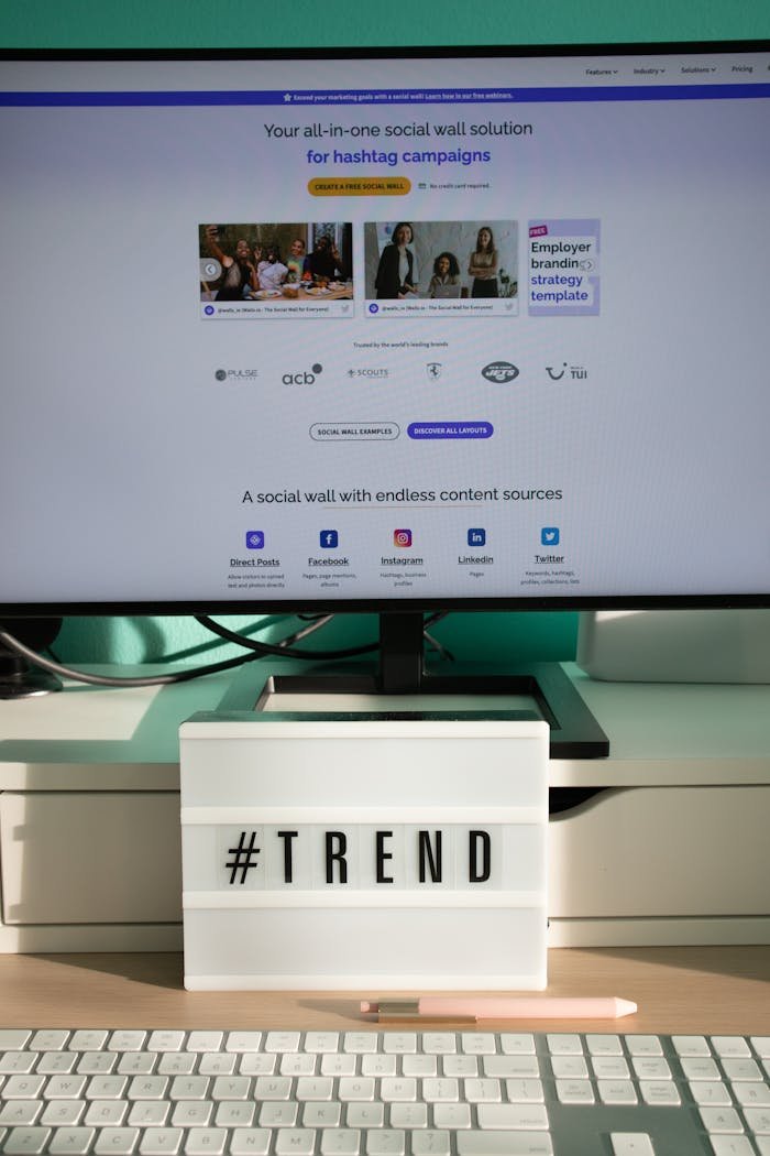 A clean and modern desk setup with a lightbox displaying #TREND and a computer monitor showing a social wall solution.